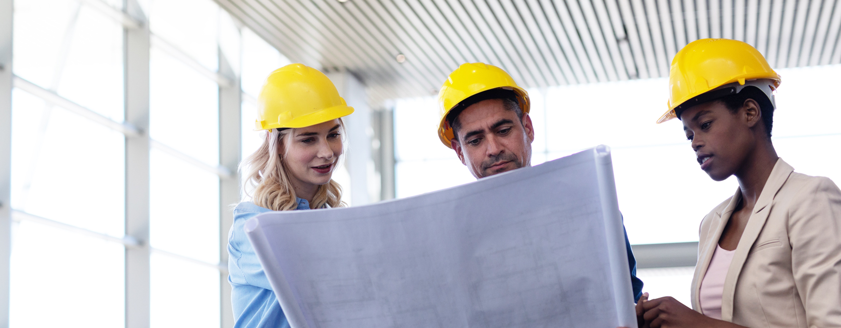 Three people in hard hats reviewing construction blueprints.